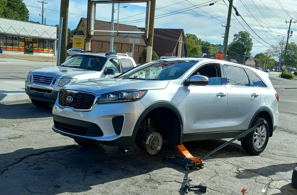 A customer's car raised on a floor jack with the wheel off in the Tire City lot
