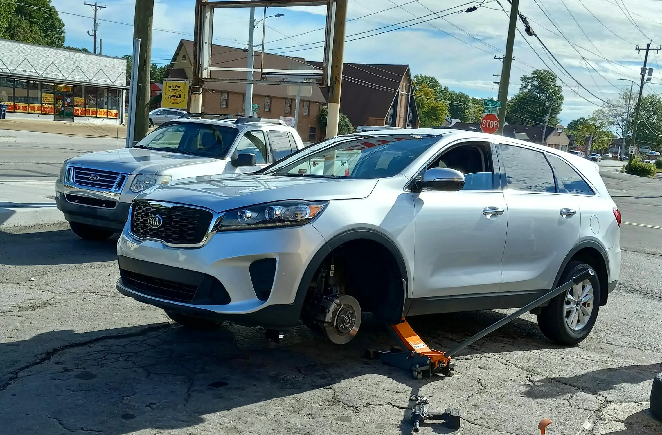 A customer's SUV on a floor jack with the wheel removed for service in Tire City's parking lot on Ringgold Road