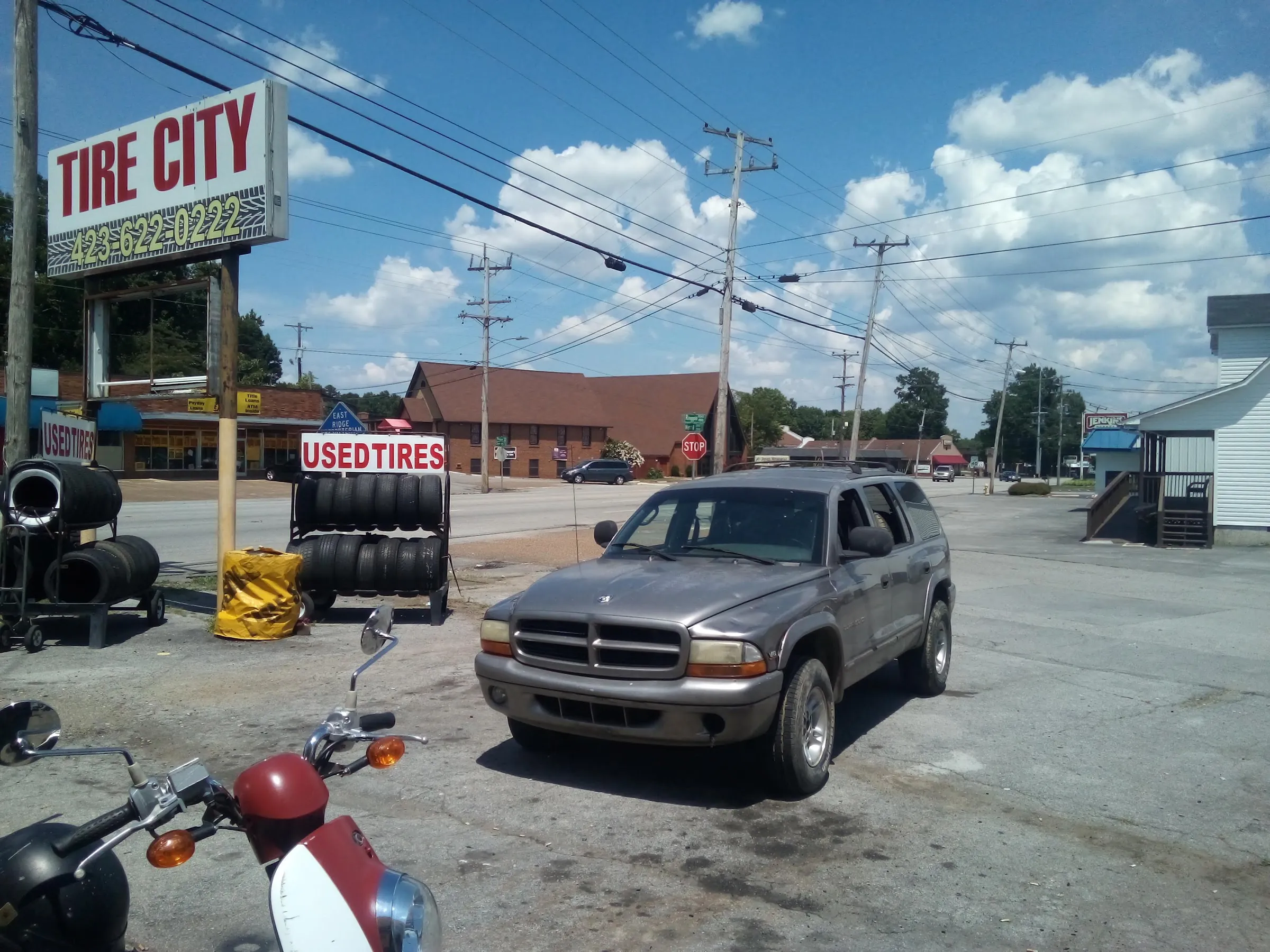 Tire City's lot with a used tire rack, a motorcycle, and a customer's SUV parked outside